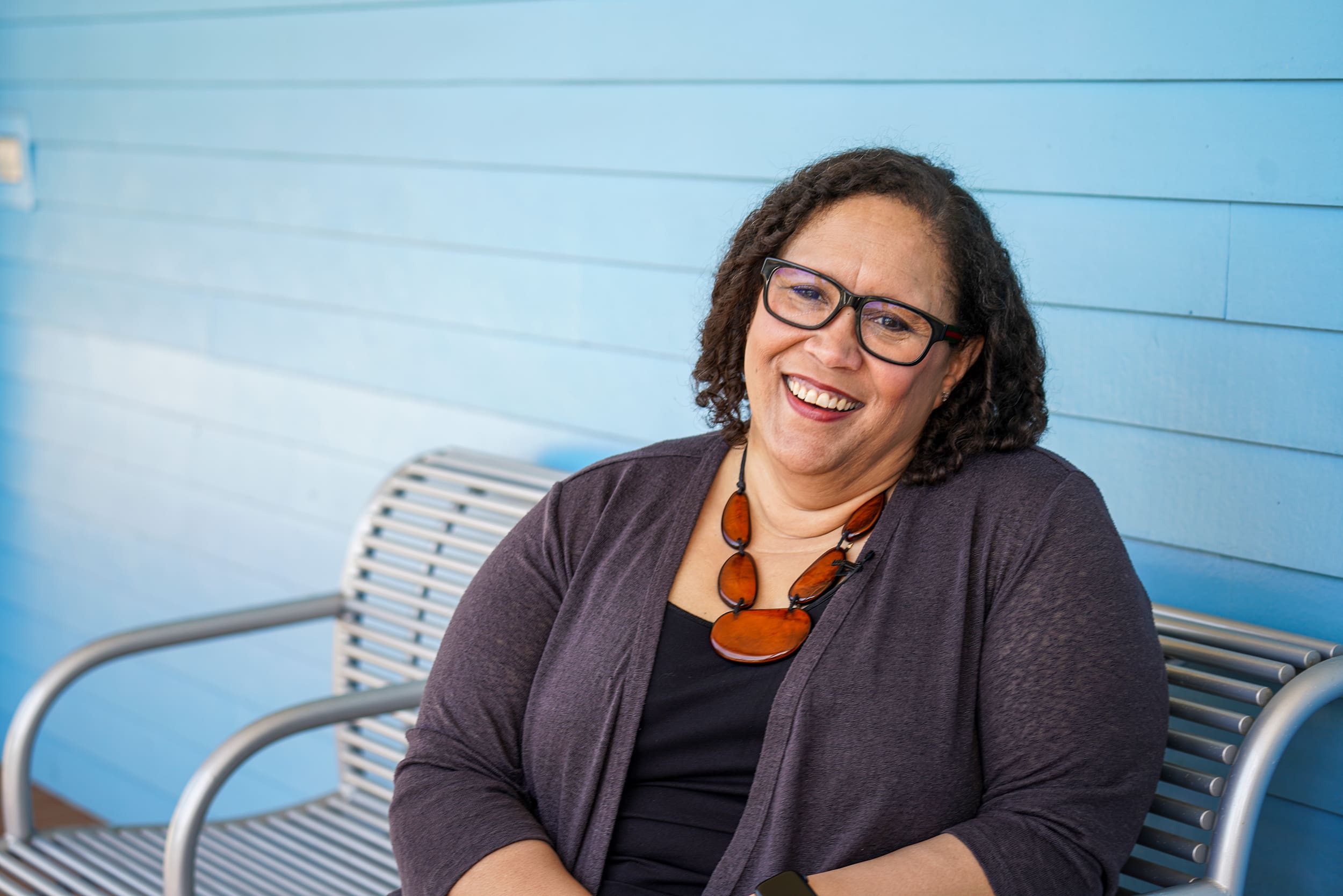 Lisa Dabney, sitting in front of a blue building, smiling.